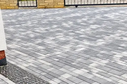 Fertig gepflasterte Hofeinfahrt aus grau nuancierten Betonpflastersteinen im Reihenverband mit dunklem Pflasterstreifen